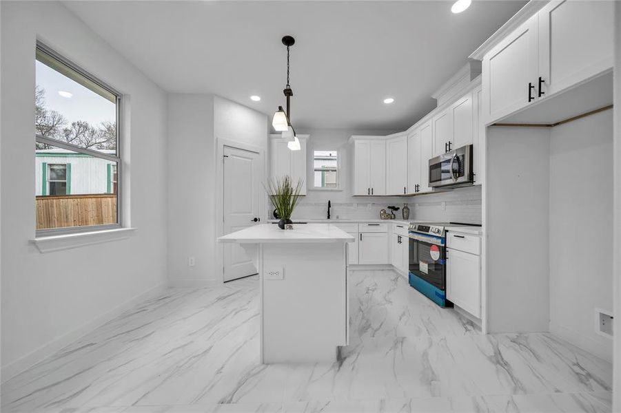 Kitchen featuring appliances with stainless steel finishes, hanging light fixtures, backsplash, white cabinets, and a kitchen island