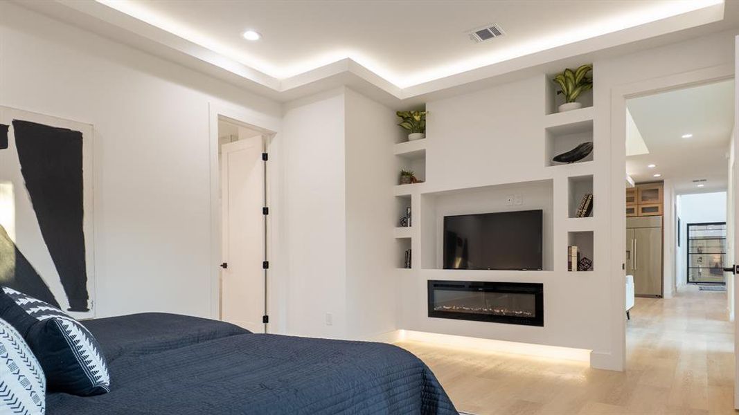 Bedroom with recessed lighting, wood finished floors, paneled refrigerator, and a glass covered fireplace
