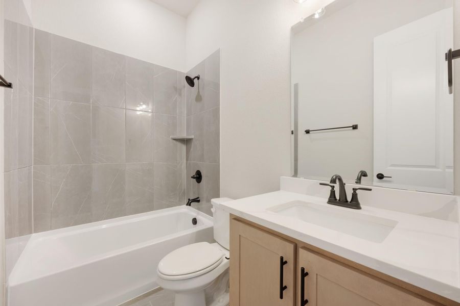 Full bathroom with tiled tub-shower combo, single vanity with white countertop, and toilet