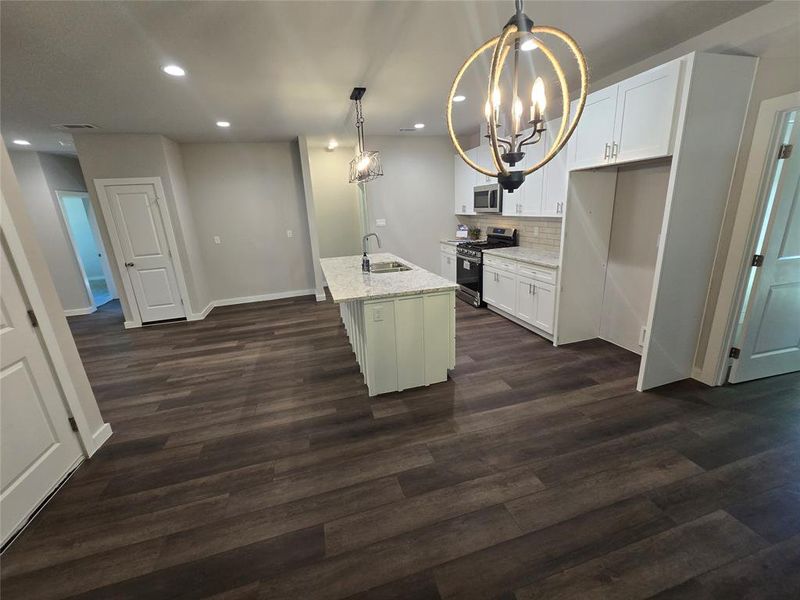 Kitchen featuring stainless steel appliances, white cabinets, a center island with sink, and decorative light fixtures