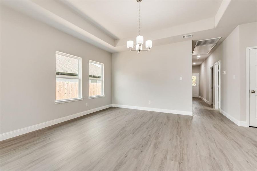 Spare room with light wood-type flooring, a tray ceiling, and an inviting chandelier