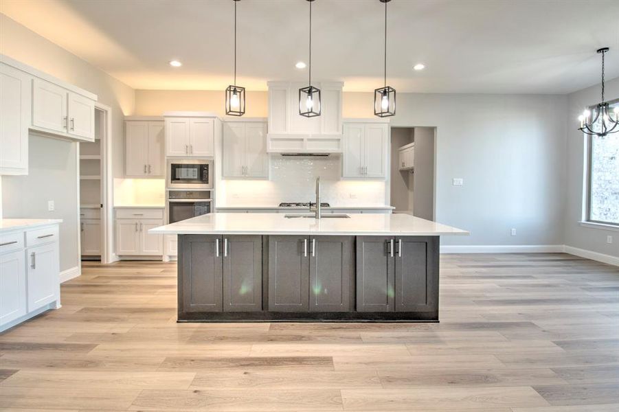 Kitchen featuring a center island with sink, oven, hanging light fixtures, and built in microwave