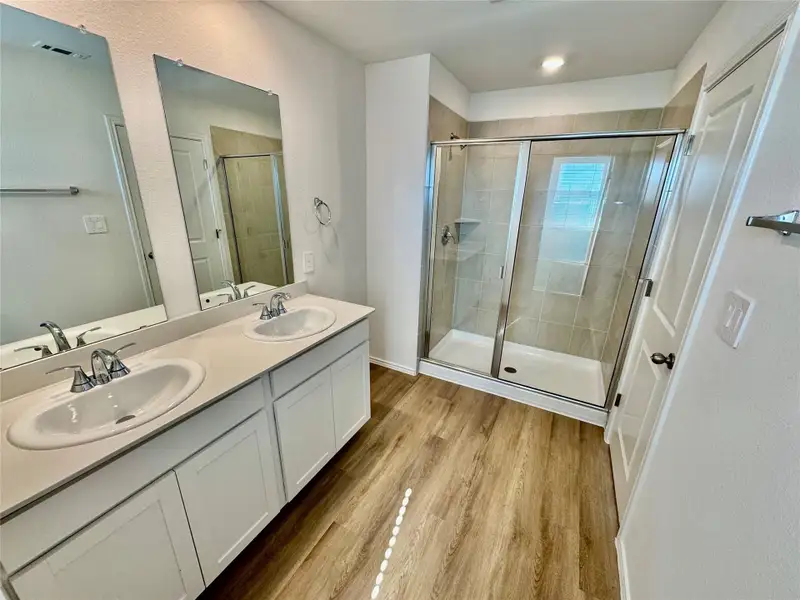 Bathroom featuring double vanity, a stall shower, light wood-style flooring, and a textured wall