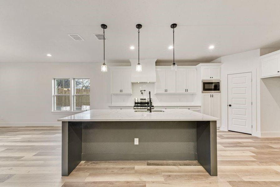 Kitchen featuring hanging light fixtures, recessed lighting, a center island with sink, a breakfast bar area, and light stone counters Kitchen featuring hanging light fixtures, recessed lighting, a center island with sink, a breakfast bar area, and light stone counters