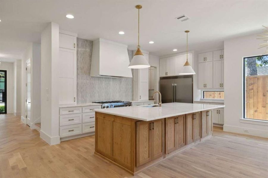 Kitchen with stainless steel appliances, a large island with sink, custom range hood, and white cabinetry