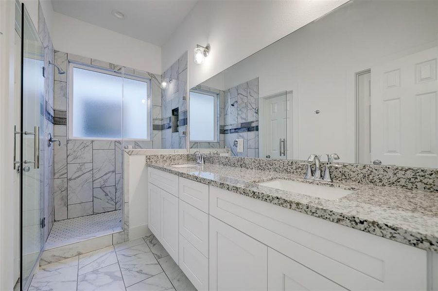 Primary bathroom boasts his and hers vanities and a glass-enclosed walk-in shower.