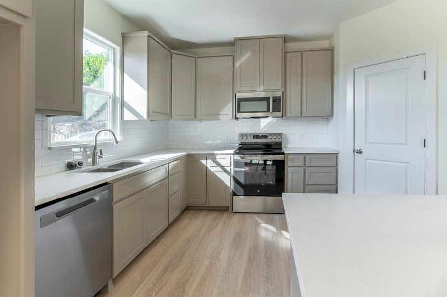 Kitchen featuring appliances with stainless steel finishes, light stone countertops, tasteful backsplash, gray cabinetry, and light wood finished floors