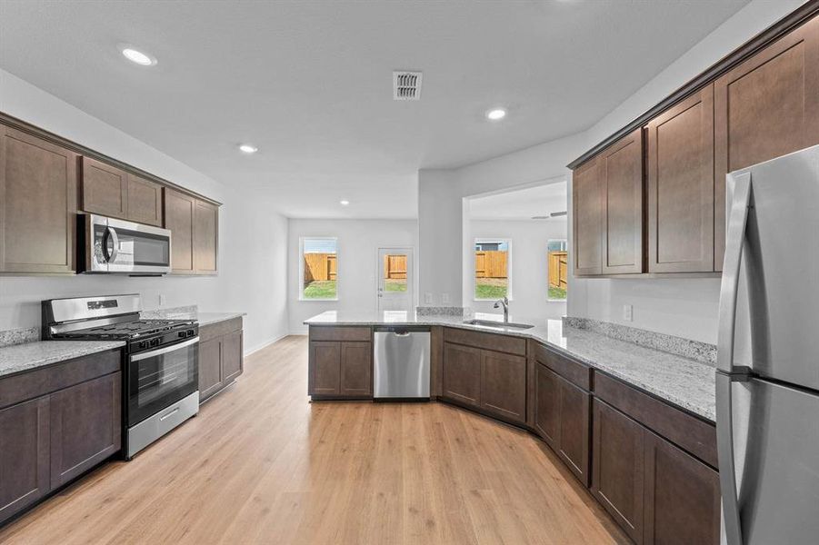 Kitchen with light wood-type flooring, kitchen peninsula, dark cabinetry, and stainless steel appliances