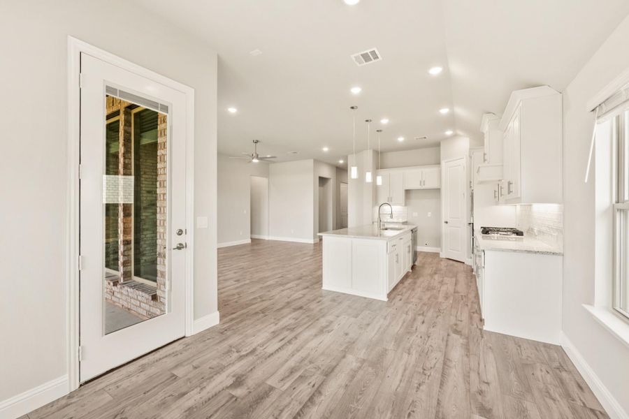 Open-concept kitchen with white cabinets, center island, and light wood floors leading to living area Open-concept kitchen with white cabinets, center island, and light wood floors leading to living area