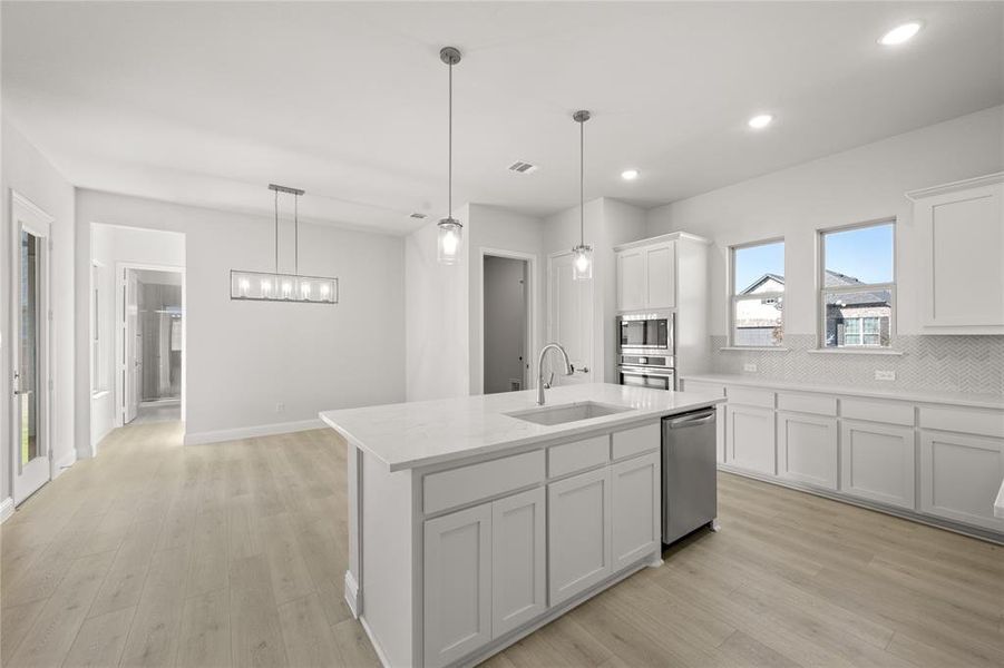 Kitchen featuring white cabinetry, sink, stainless steel appliances, pendant lighting, and a kitchen island with sink