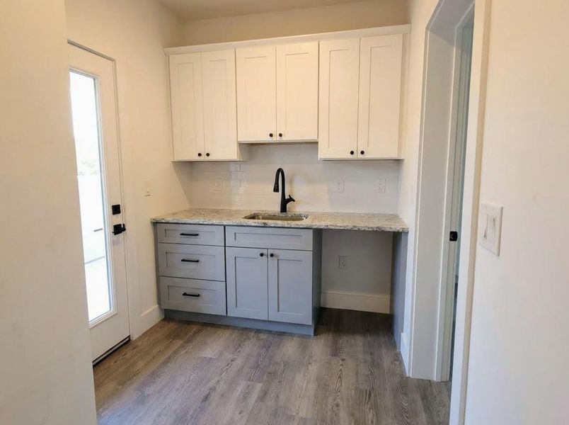 Kitchen with gray cabinets, white cabinetry, light stone countertops, dark wood-type flooring, and backsplash