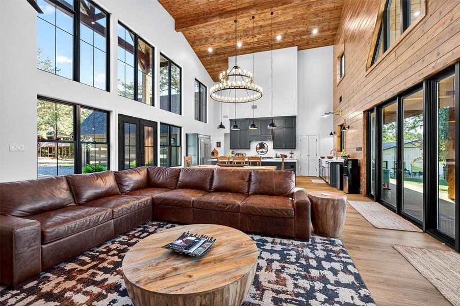 Living room featuring a wood ceiling with exposed beams, light wood finished floors, a towering ceiling, a chandelier, and recessed lighting Living room featuring a wood ceiling with exposed beams, light wood finished floors, a towering ceiling, a chandelier, and recessed lighting