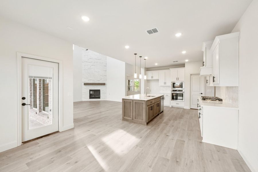 Open-concept kitchen with white cabinets, center island, and light wood floors flowing into living area with fireplace Open-concept kitchen with white cabinets, center island, and light wood floors flowing into living area with fireplace