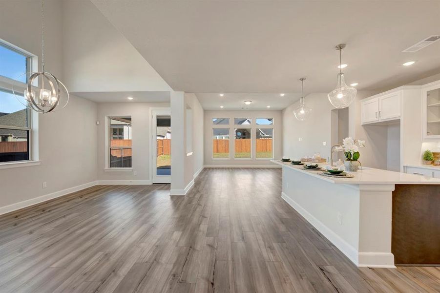 Kitchen featuring white cabinetry, open floor plan, an island with sink, glass fronted cabinets, and light wood-style floors