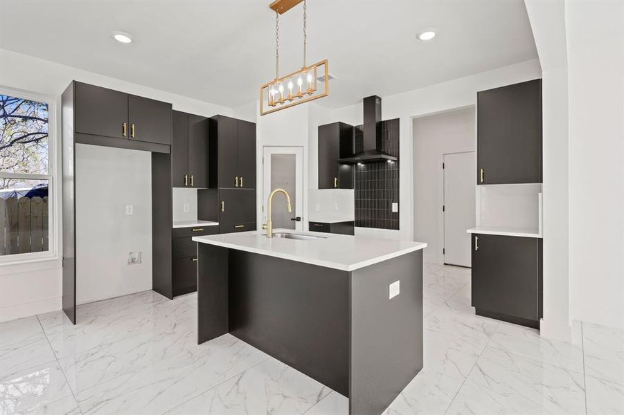 Kitchen with decorative light fixtures, sink, a kitchen island with sink, and wall chimney range hood