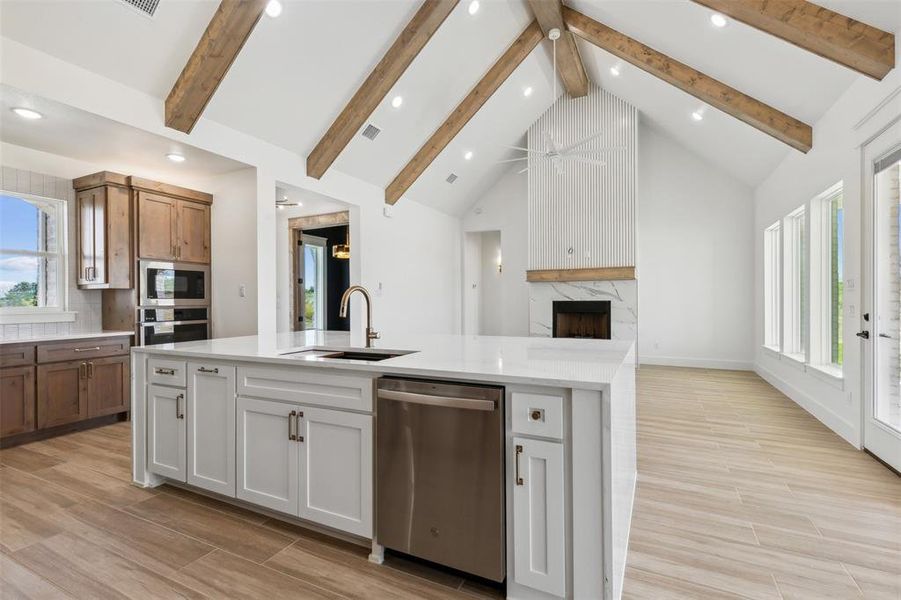 Kitchen with white cabinets, stainless steel appliances, beamed ceiling, sink, and a high end fireplace