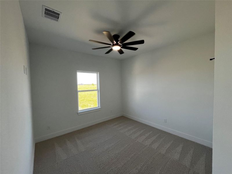 The secondary room features neutral walls, a ceiling fan, and a window with a view of a grassy outdoor area, creating a bright and airy space.