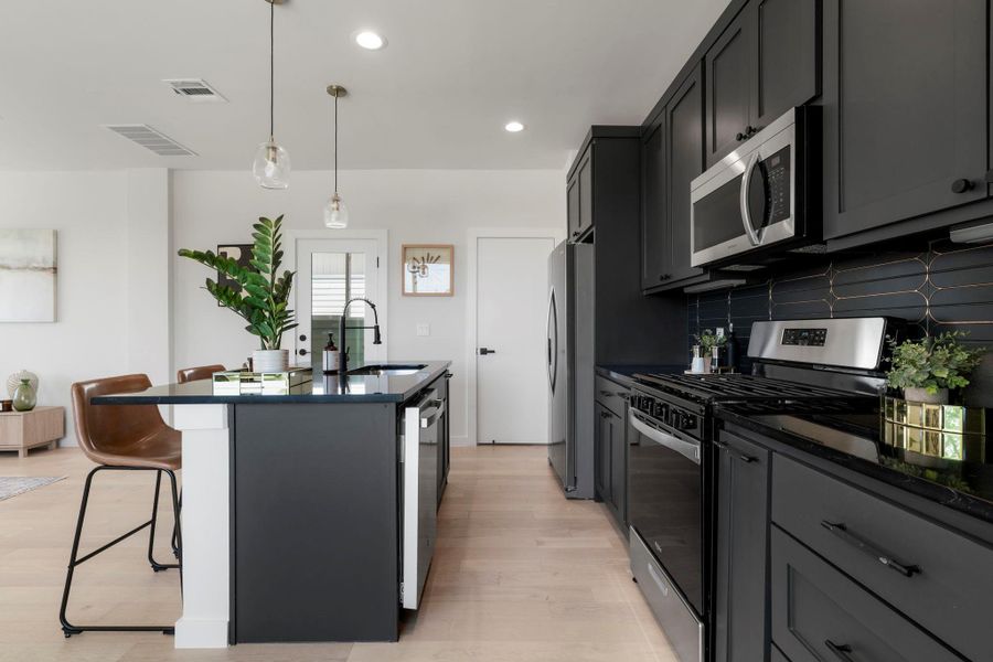 Kitchen featuring stainless steel appliances, a breakfast bar area, hanging light fixtures, dark stone counters, and tasteful backsplash