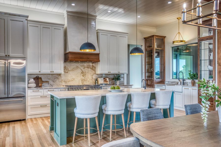 Kitchen with high end fridge, a kitchen island with sink, backsplash, premium range hood, and decorative light fixtures Kitchen with high end fridge, a kitchen island with sink, backsplash, premium range hood, and decorative light fixtures