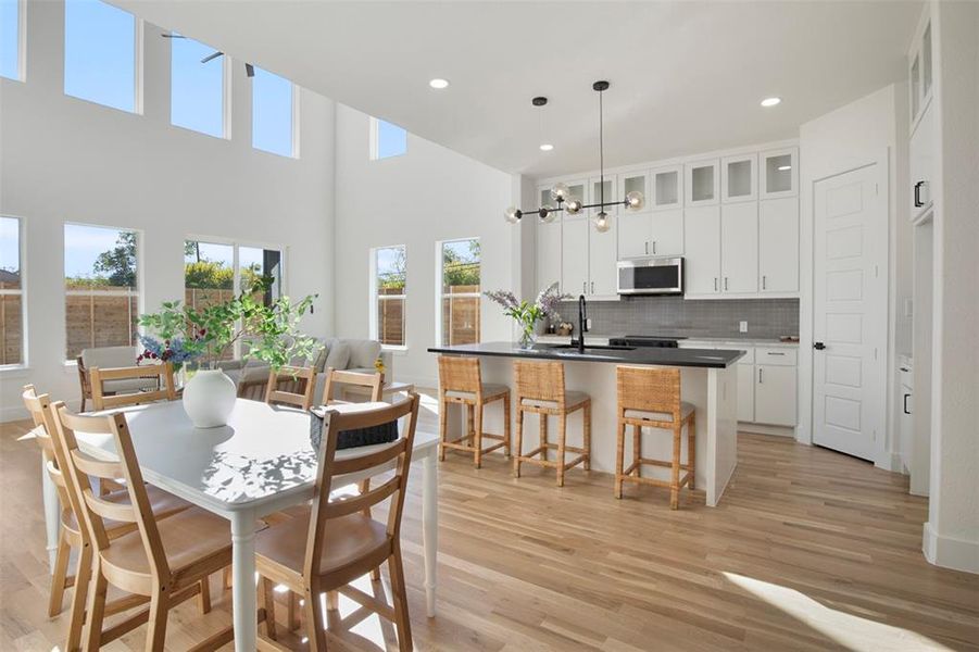 Dining room with a towering ceiling, an inviting chandelier, light hardwood / wood-style flooring, and sink