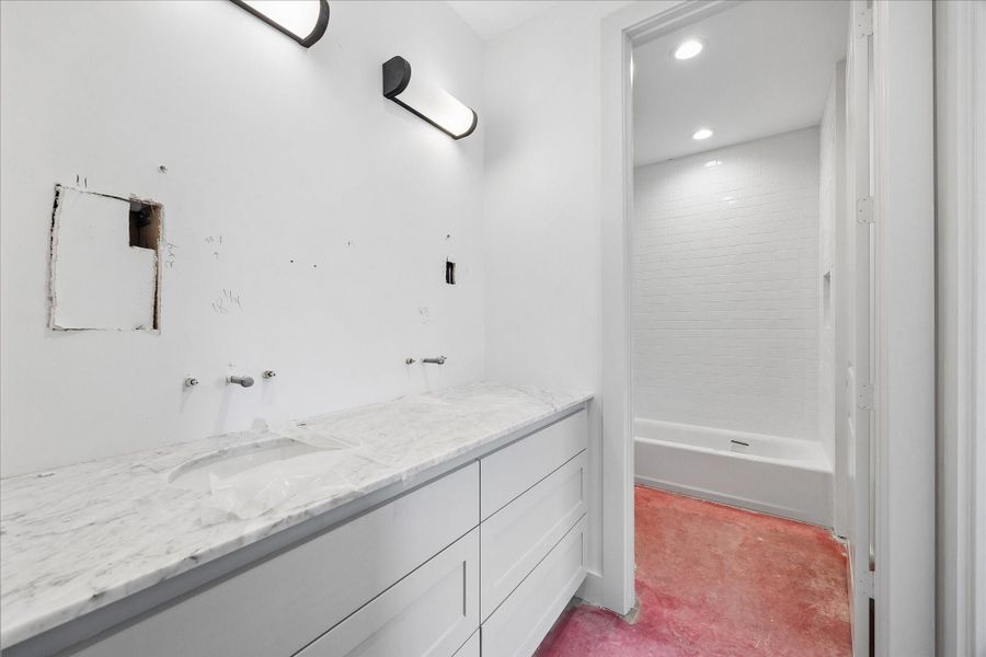 Spacious Jack and Jill bathroom designed with functionality in mind, featuring an extended dual vanity with generous counter space and ample storage below. The layout flows into a separate tub and shower area finished with classic white subway tile, offering privacy and convenience for shared use. Clean lines and a neutral palette create a bright, timeless foundation ready for final touches.