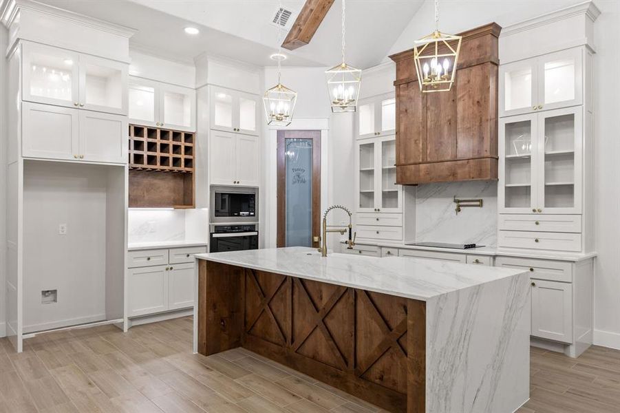 Spacious kitchen featuring an oversized island with waterfall countertop, custom wood cabinetry, stainless steel appliances, and wood-finish flooring Spacious kitchen featuring an oversized island with waterfall countertop, custom wood cabinetry, stainless steel appliances, and wood-finish flooring