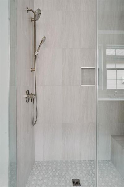 Walk-in shower featuring large format tiled walls, a hex mosaic tiled floor, and a built-in shower bench Walk-in shower featuring large format tiled walls, a hex mosaic tiled floor, and a built-in shower bench