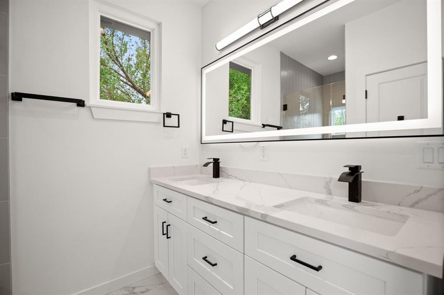 Full bathroom featuring double vanity, a shower stall, and light marble finish flooring
