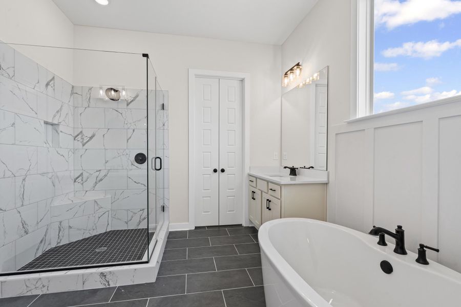 Bathroom featuring a marble finish shower, vanity, a soaking tub, dark tile patterned flooring, and a closet Bathroom featuring a marble finish shower, vanity, a soaking tub, dark tile patterned flooring, and a closet