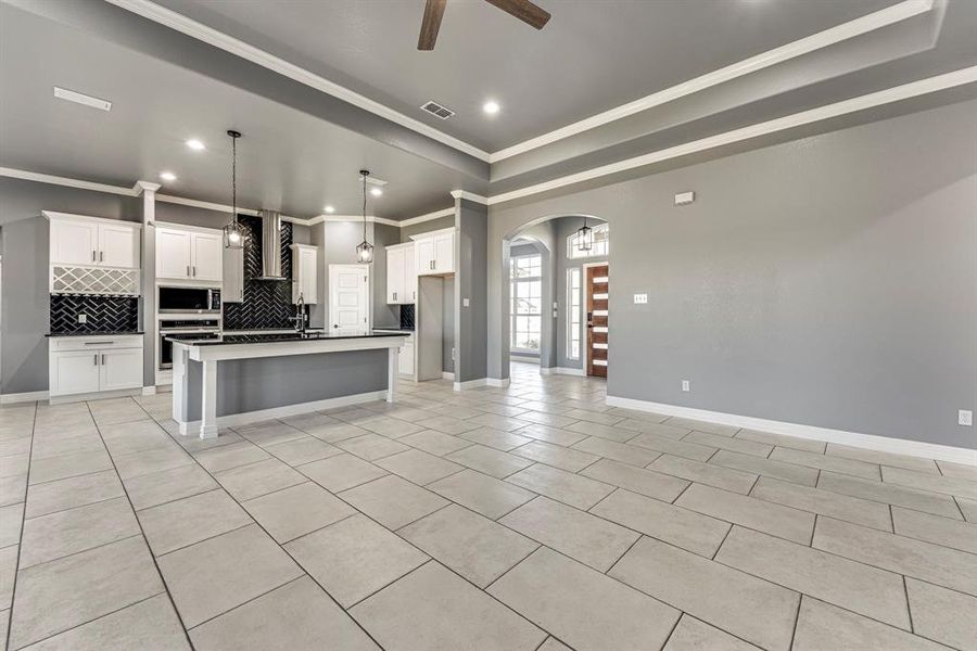 Kitchen with pendant lighting, a kitchen island with sink, white cabinets, wall chimney exhaust hood, and appliances with stainless steel finishes