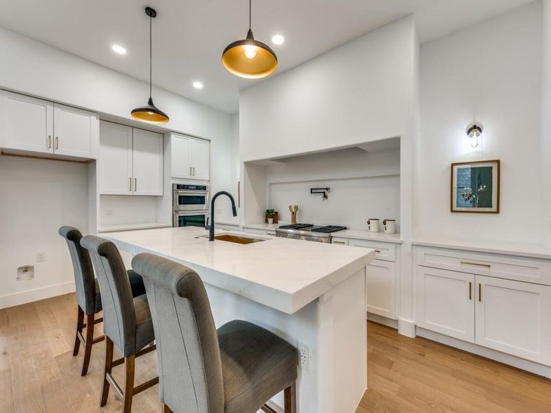 Kitchen featuring light stone counters, pendant lighting, an island with sink, white cabinetry, and light hardwood / wood-style flooring