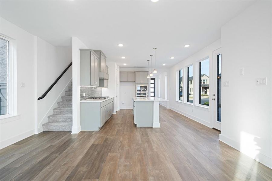 Kitchen featuring gray cabinetry, decorative backsplash, pendant lighting, a kitchen island with sink, and hardwood / wood-style flooring