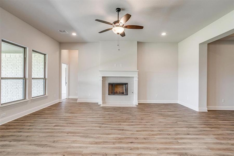 Unfurnished living room with a tiled fireplace, light wood-type flooring, and ceiling fan