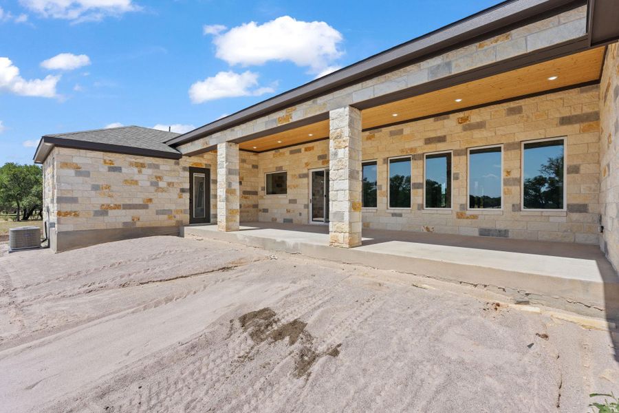 A newly constructed home featuring an elevated covered patio with stone columns and a wood-planked ceiling. A newly constructed home featuring an elevated covered patio with stone columns and a wood-planked ceiling.