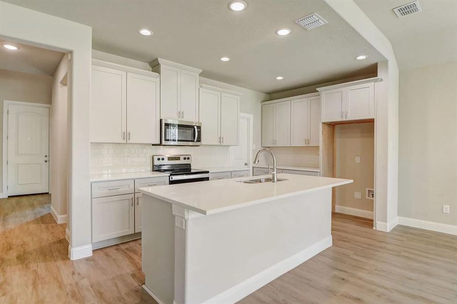 Kitchen featuring stainless steel appliances, a sink, light wood-style flooring, a kitchen island with sink, and recessed lighting