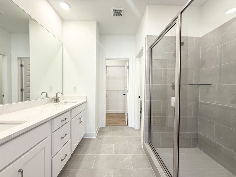 Bathroom featuring double vanity, a shower stall, a spacious closet, light tile patterned floors, and recessed lighting
