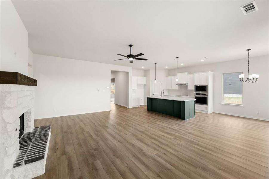 Unfurnished living room with light wood-style flooring, suspended lighting, ceiling fan, and a stone fireplace