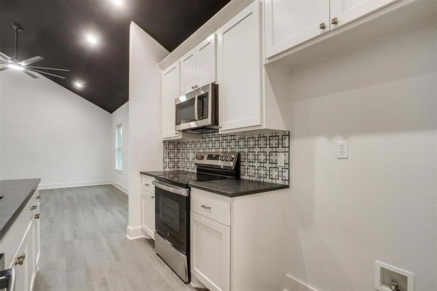 Kitchen featuring appliances with stainless steel finishes, ceiling fan, decorative backsplash, light wood-style floors, and white cabinetry