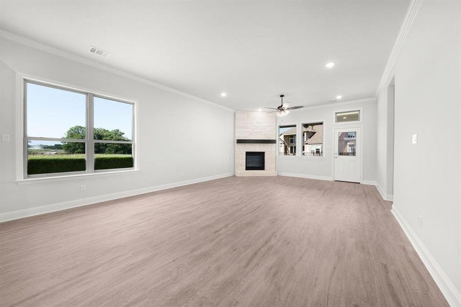 Large living room featuring crown molding, ceiling fan, a stone fireplace, luxury vinyl flooring, and recessed lighting