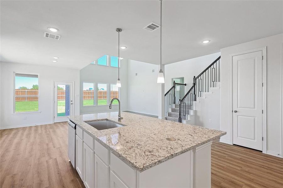 Kitchen with pendant lighting, a kitchen island with sink, sink, white cabinets, and light hardwood / wood-style flooring