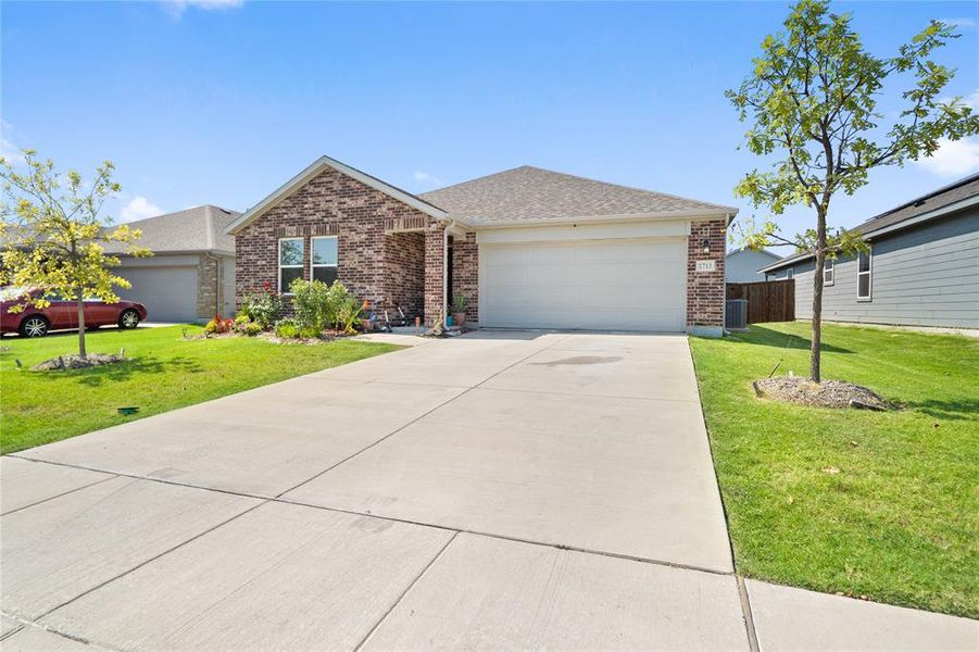 View of front facade featuring a front lawn, brick siding, a garage, roof with shingles, and concrete driveway