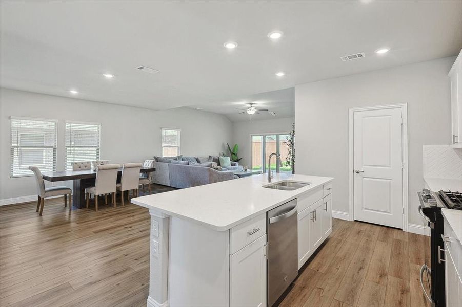 Kitchen featuring sink, gas range, light wood-type flooring, and white cabinetry