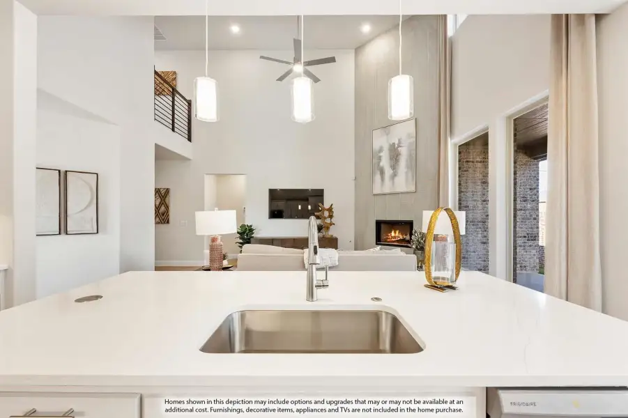 Kitchen island with undermount sink and pendant lights, open to living room with fireplace and two-story ceiling