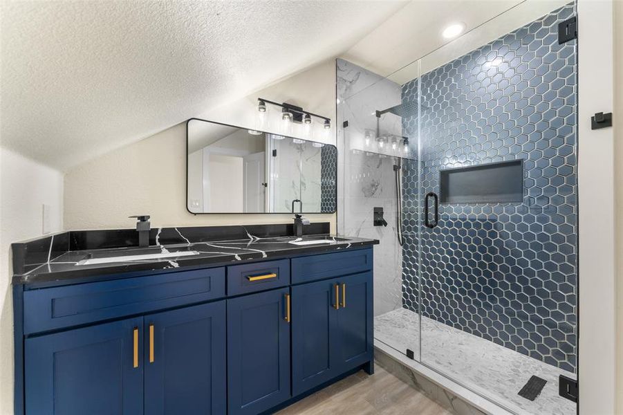 Full bath with a shower stall, double vanity, a textured ceiling, wood finished floors, and vaulted ceiling