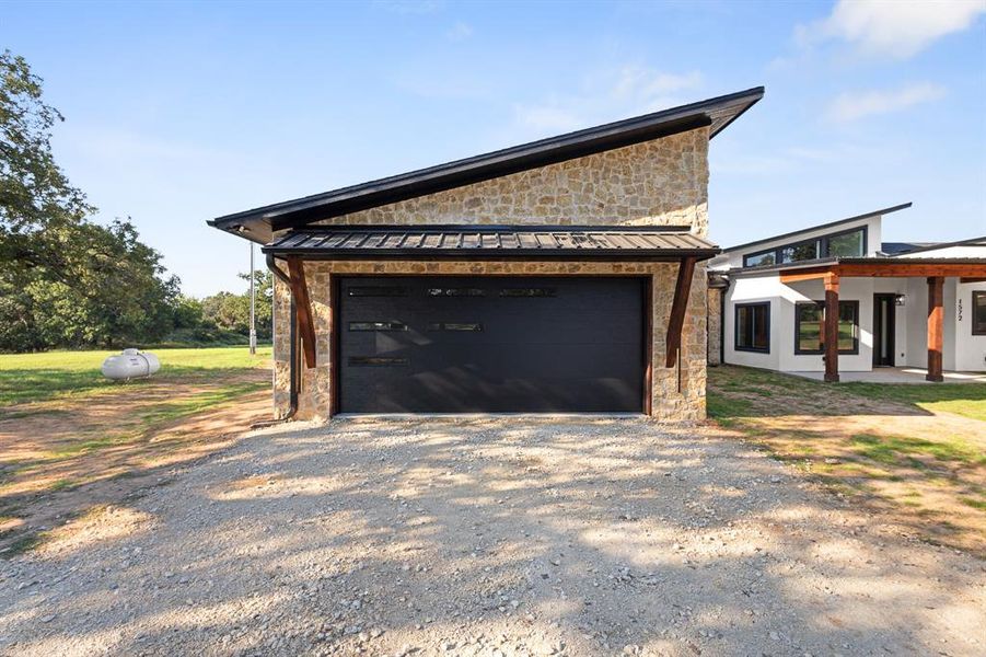View of property exterior featuring stone siding, a garage, a metal roof, and a standing seam roof