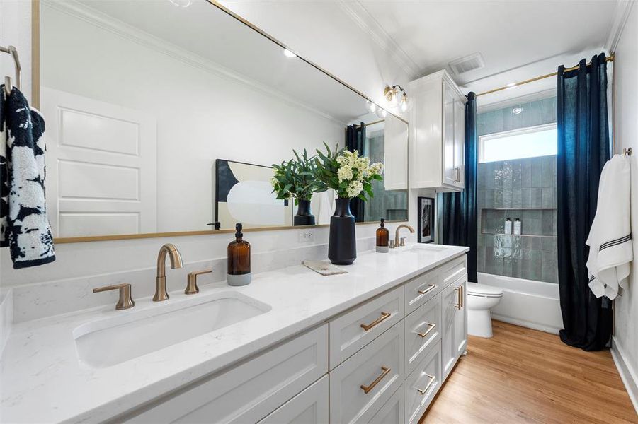 Full bath with ornamental molding, double vanity, wood finished floors, and shower / bathtub combination