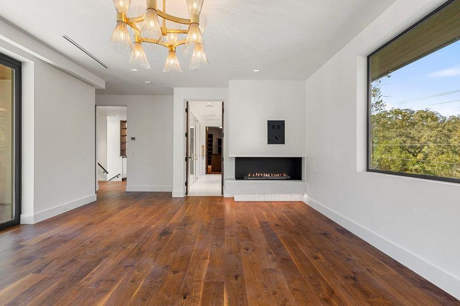Unfurnished living room featuring a lit fireplace, dark wood-type flooring, and a chandelier