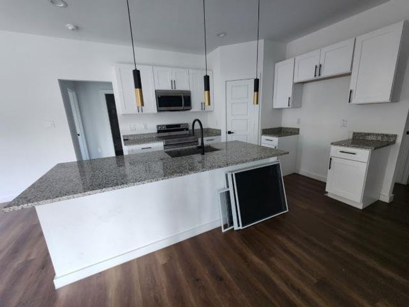 Kitchen featuring dark wood-style floors, white cabinetry, dark stone countertops, stainless steel microwave, and pendant lighting Kitchen featuring dark wood-style floors, white cabinetry, dark stone countertops, stainless steel microwave, and pendant lighting