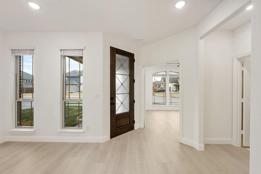 Bright entryway with dark wood glass-panel front door, light hardwood floors, and white walls with arched hallway opening Bright entryway with dark wood glass-panel front door, light hardwood floors, and white walls with arched hallway opening