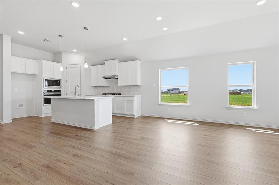 Kitchen featuring white cabinetry, a kitchen island with sink, stainless steel appliances, light wood-style floors, and open floor plan